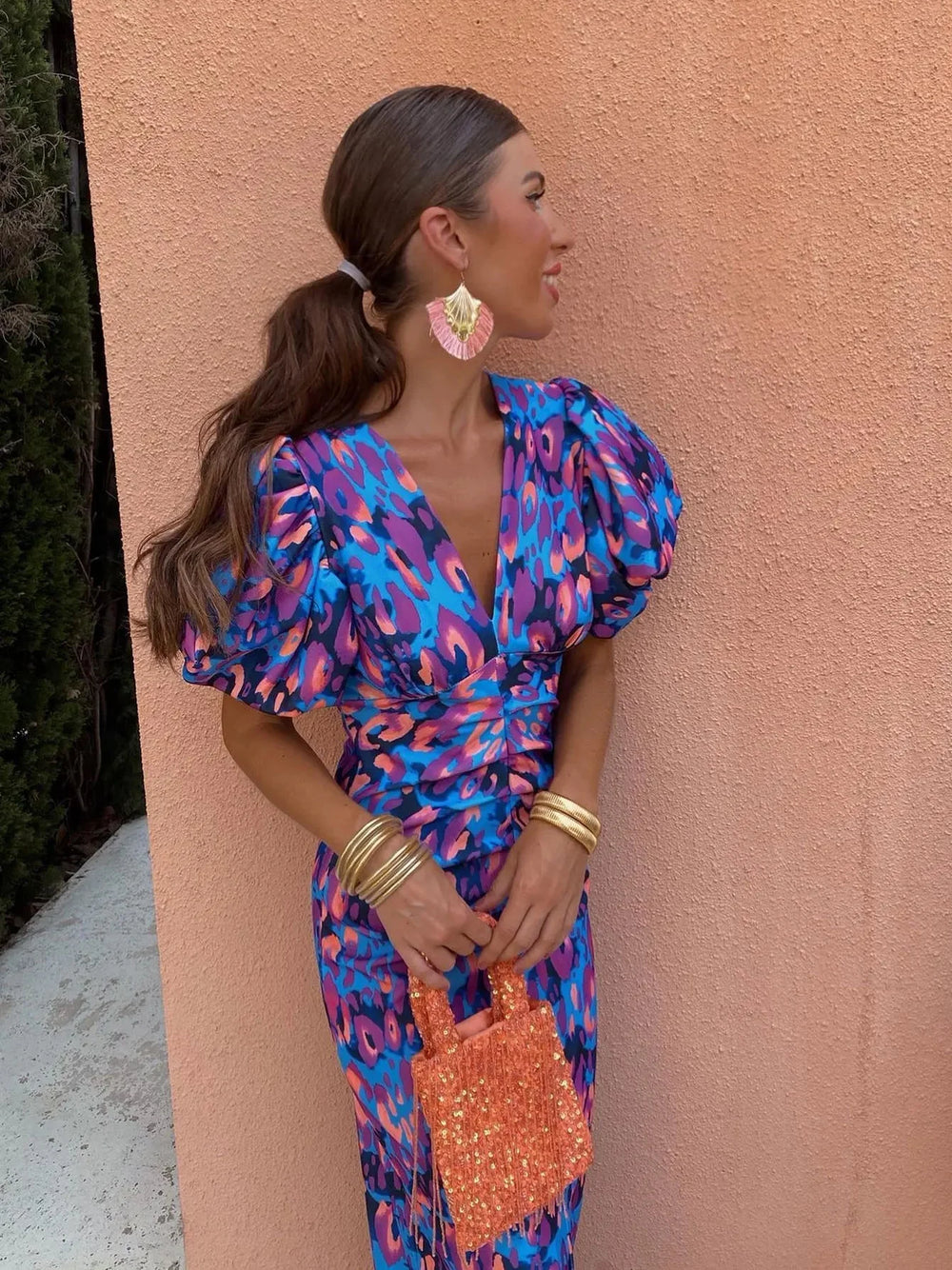 Women's cocktail dress in a blue and purple floral pattern with puff sleeves, V-neck, and cinched waist, styled with gold bangles.