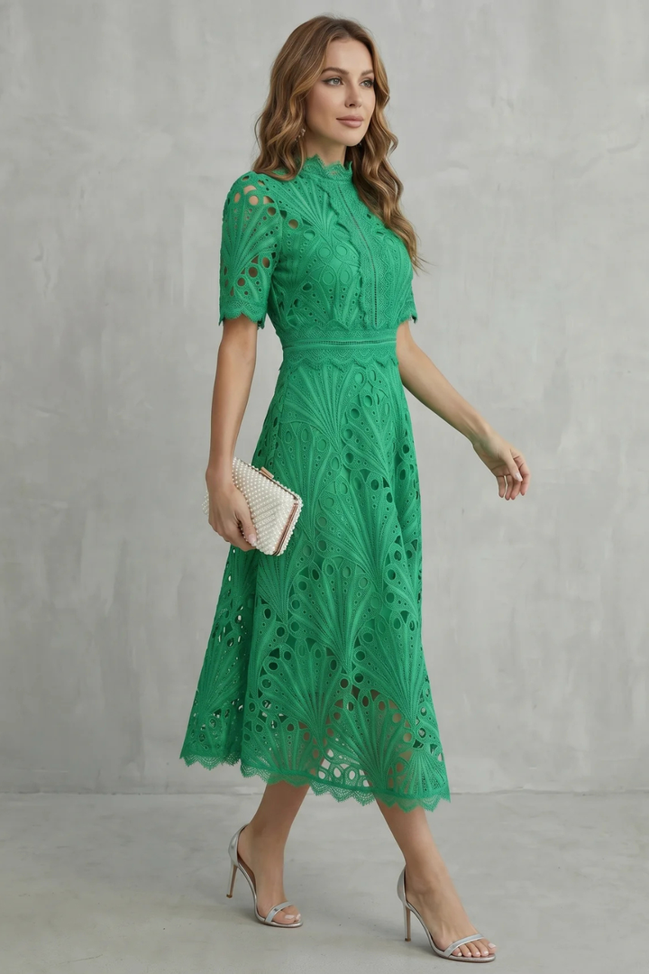 Side view of green wedding guest lace midi dress with high neck and fitted waist, worn with silver heels